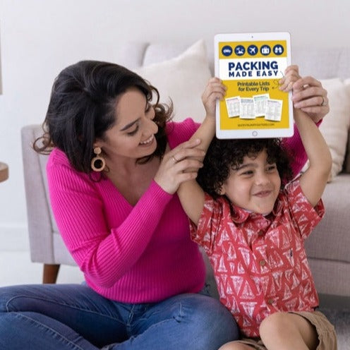 Boy and mom holding up printable packing lists on tablet to get ready to pack for family vacation.